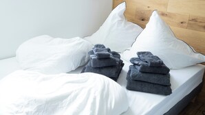 Ein Bett mit weißer Bettwäsche und Kissen, ein hölzernes Kopfende und gefaltete Handtücher.