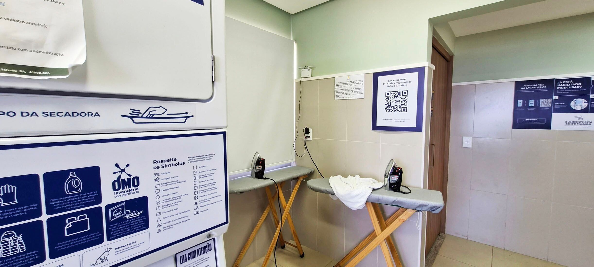 A hotel bathroom with a hand dryer, a towel rack, a mirror, and a QR code on the wall.