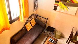 Una habitación con sofá, una mesita, una silla, una ventana con cortinas y un cuadro en la pared.