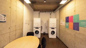 A laundry room with two washing machines, a table, chairs, and informational posters on the wall.