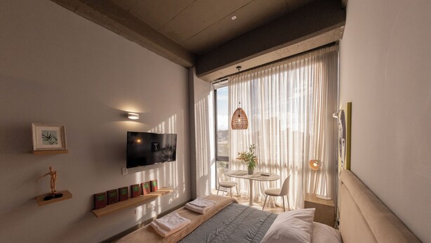 A modern hotel room with a bed, TV, and a balcony with a table and chairs. - Artistic Hub / Gourmet District Loft, Chapinero Alto (Bogotá)