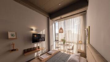 Une chambre d’hôtel moderne équipée d’un lit, d’une télévision et d’un balcon avec une table et des chaises.
