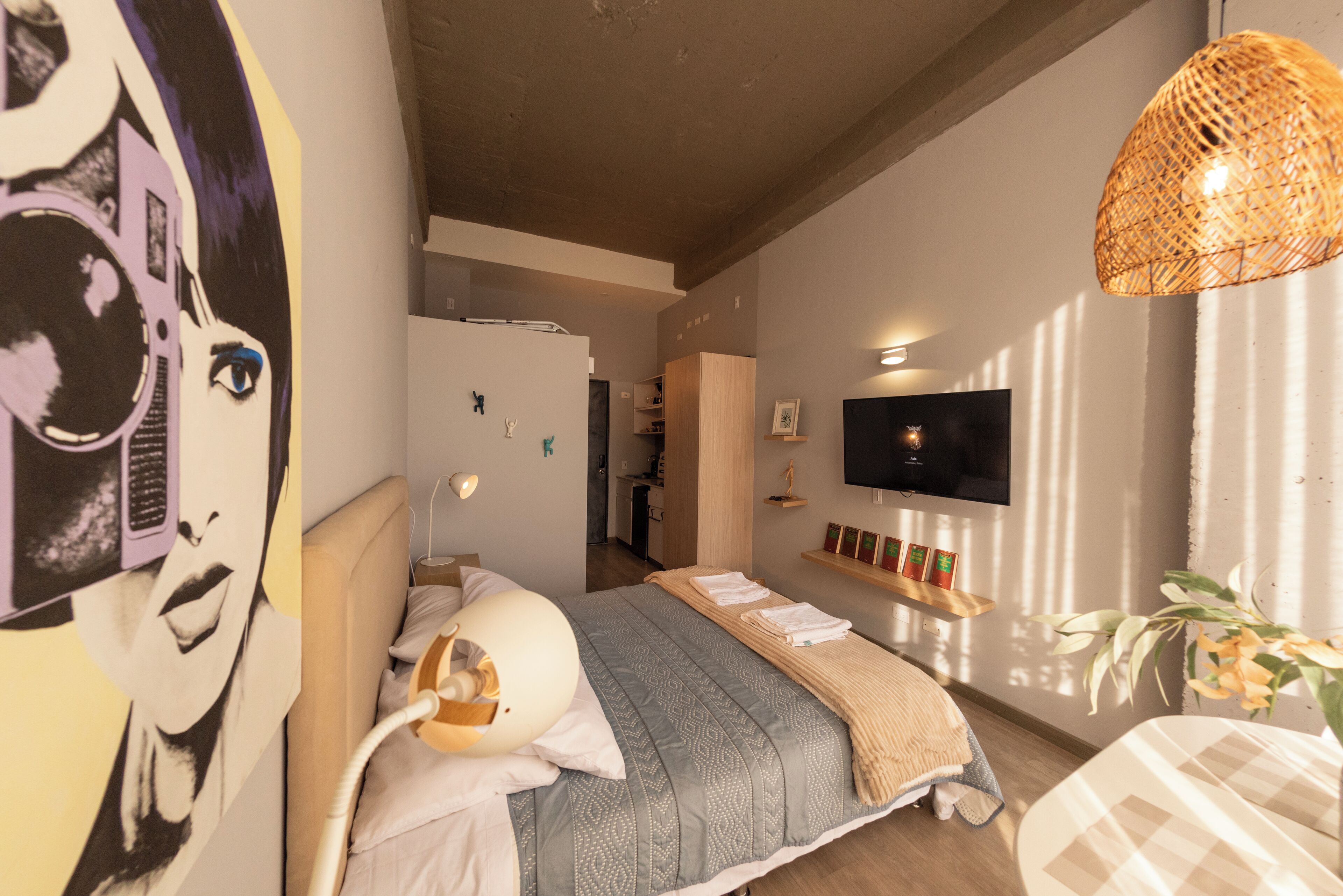 Ein Schlafzimmer mit einem Bett, einem an der Wand montierten Fernseher, einer Nachttischlampe und einem Wandbild.