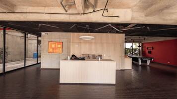 A reception desk in a modern building with a concrete ceiling, a wooden reception desk, a hanging light fixture, and a billiards table.