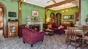 A room with a fireplace, a television, a bookshelf, a dining table with chairs, and a ceiling fan. - The Kirkhouse Bed and Breakfast (Friday Harbor)