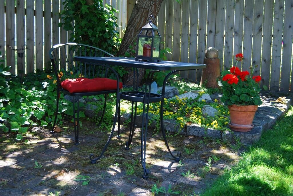 A garden setting with a metal table and chair, a lantern, and potted plants.