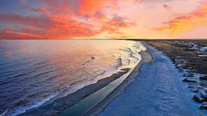 Une plage au coucher du soleil, avec une eau calme et une côte lointaine.