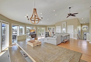 A spacious living area with a large wooden dining table, a sofa, and a chandelier. - 7BR IOP Luxury - Porches, Pool, Spa and Ocean Views (Isle of Palms)