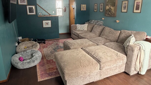 Ein Wohnzimmer mit einer Eckcouch, einem Flachbildfernseher und einem großen Fenster.