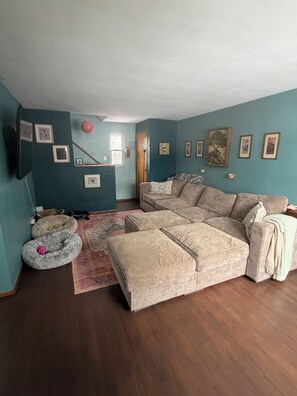 A living room with a sectional sofa, a flat-screen TV, and a large window. - Inviting & Cozy 2 Bedroom Home in Pittsburgh (Pittsburgh)