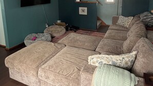 Ein Wohnzimmer mit einem großen Ecksofa, einem Flachbildfernseher an der Wand und einer Treppe, die zu einer weiteren Ebene führt.