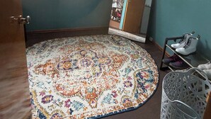 Ein Zimmer mit türkisfarbenen Wänden, einem gemusterten Teppich, einem Fenster, einem Spiegel und einem Schuhregal.