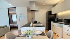 A modern kitchen with a central island, dining table set for two, and a sofa in the living area.