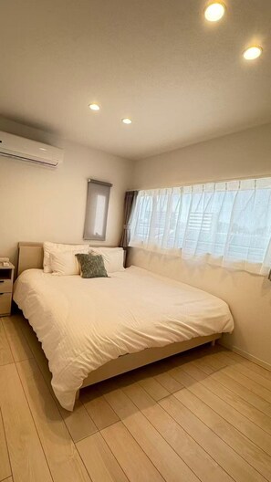 A bedroom with a bed, a nightstand, a window with curtains, and an air conditioning unit. - Akikawa Ozu 1 | 15 min to TSMC | Entire 3LDK House | Up to 6 Guests (Ozu)