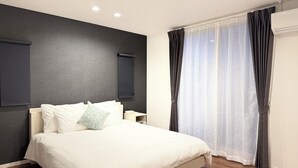 A bedroom with a bed, a nightstand, a wall-mounted air conditioner, and a window with curtains. - Akikawa Ozu 1 | 15 min to TSMC | Entire 3LDK House | Up to 6 Guests (Ozu)