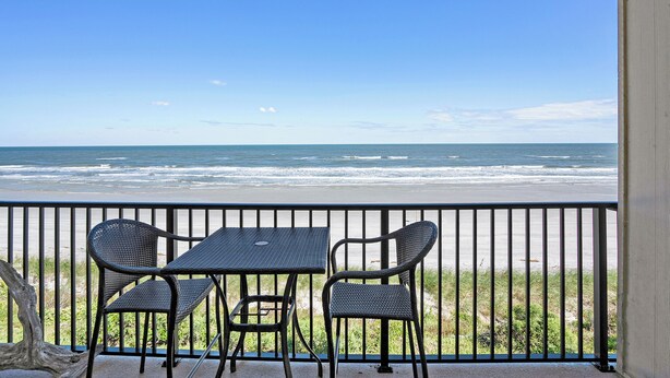 Ein Balkon mit zwei Stühlen und einem Tisch mit Blick auf den Strand.