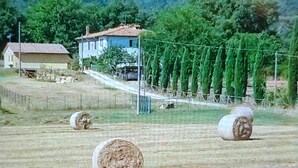 Paisagem rural com fardos de feno, uma casa e uma cerca.