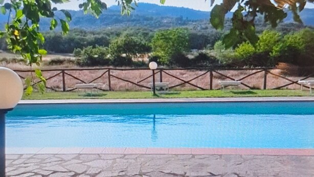 Piscina com deck de pedra, cerca de metal e vista para uma paisagem montanhosa.