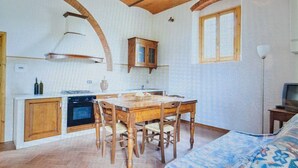 Uma cozinha compacta com mesa de jantar, cadeiras de madeira, forno embutido e uma janela.