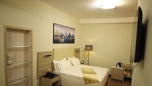 Una habitación de hotel con cama, mesitas de noche, lámpara, un cuadro y televisor.