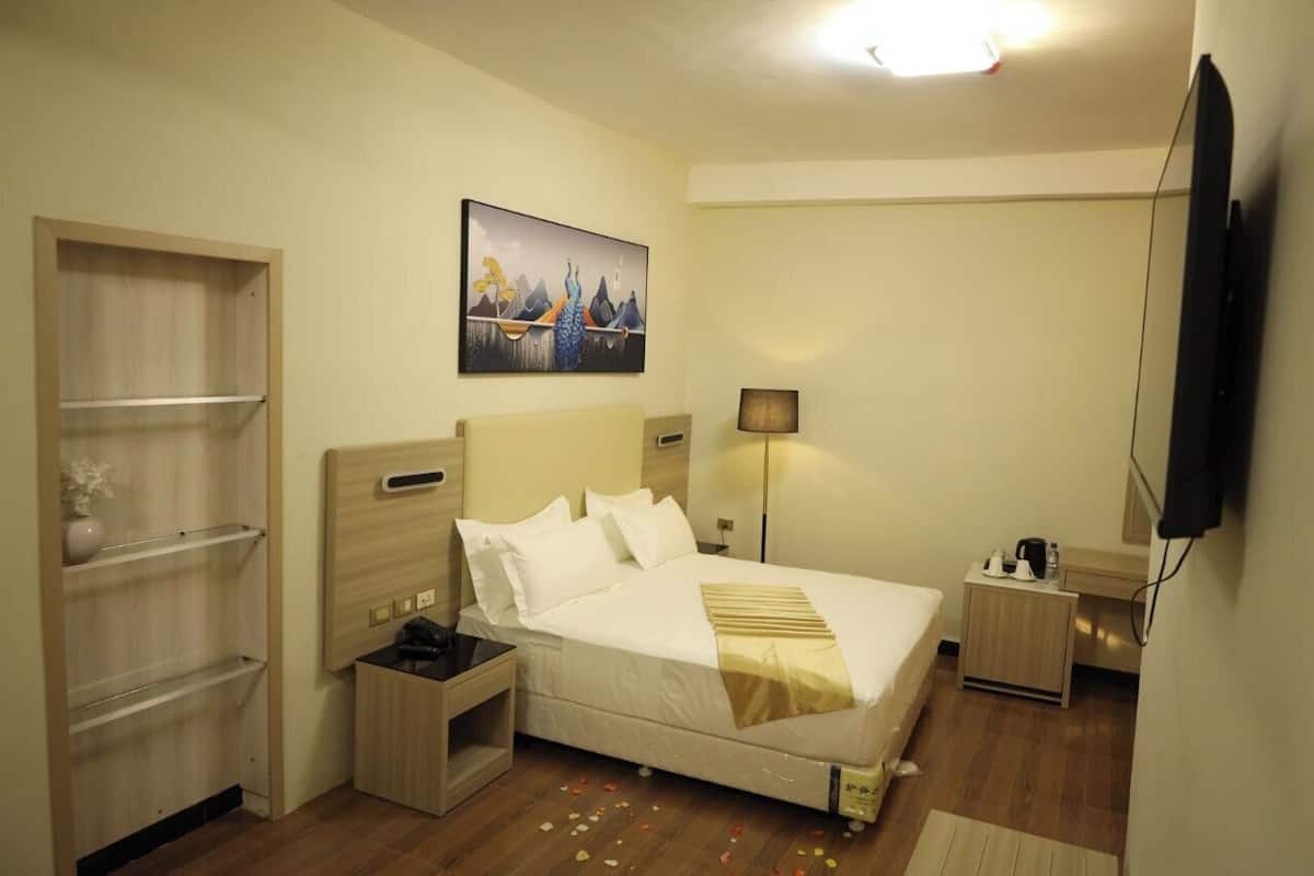 Ein Hotelzimmer mit Bett, Nachttischen, einer Lampe, einem Gemälde und einem Fernseher.