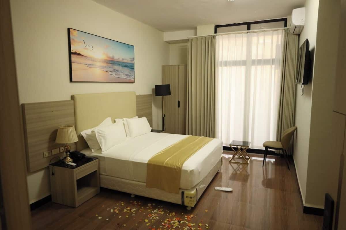 Ein Hotelzimmer mit Bett, Nachttisch, Lampe und einem Bild an der Wand.