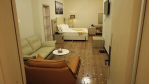 Una habitación de hotel con cama, sofá, una mesita, televisor y lámpara.