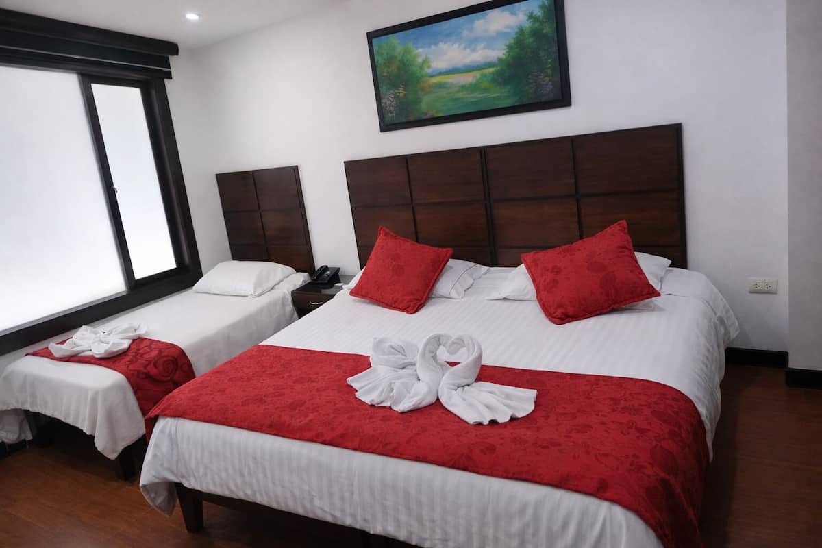 Ein Hotelzimmer mit zwei Betten, roter und weißer Bettwäsche, einem Bild an der Wand und einem Fenster mit Jalousien.