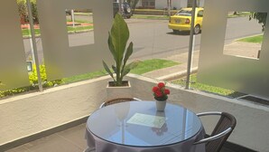 Een tafel met glazen blad, twee stoelen, een bloempot en een klein tafeltje met een menukaart.
