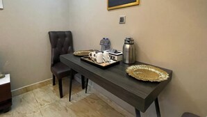 Ein Essbereich mit einem dunklen Holztisch, einem einzelnen braunen Stuhl, einer Serviertablett mit weißen Tassen und einem Thermos sowie einem gerahmten Stadtbild an der Wand.
