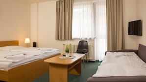 A hotel room with two beds, a desk, a chair, a radiator, and a TV. - Hotel Kanarek (Prague)