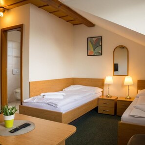 A hotel room with a wooden bed, bedside lamps, a small table with a remote control, and a potted plant. - Hotel Kanarek (Prague)