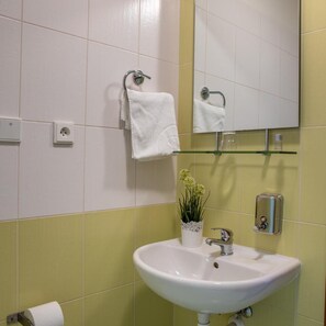 A bathroom with a white sink, a mirror, a towel rack, a glass shelf, and a potted plant. - Kanarek Hotel (Prague)