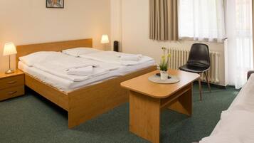 Habitación de hotel con cama, mesita de noche, lámpara, silla y una pequeña mesa con una planta en maceta.