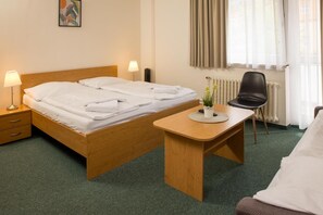 A hotel room with a bed, bedside table, lamp, chair, and a small table with a potted plant. - Hotel Kanarek (Prague)