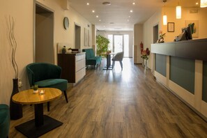 A hotel lobby with a reception desk, seating area, and a view of the outdoors. - Hotel Kanarek (Prague)