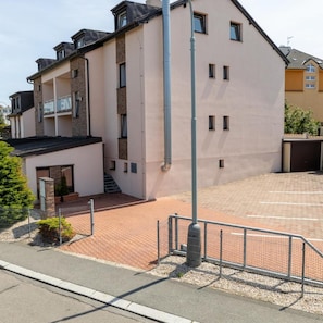 Un immeuble à plusieurs étages, doté d’un toit plat, d’un espace de stationnement et d’une entrée sécurisée par un portail.