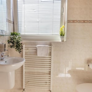 A bathroom with a sink, a towel rack, a radiator, and a window with blinds. - Hotel Kanarek (Prague)