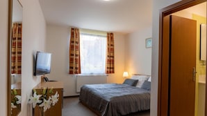 A hotel room with a bed, a desk with a computer, a television, and a window with curtains. - Hotel Kanarek (Prague)