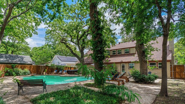 Un patio trasero con piscina, banco y una casa.
