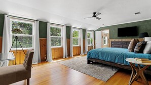 Un dormitorio con cama, escritorio, silla, televisor y ventanas amplias.