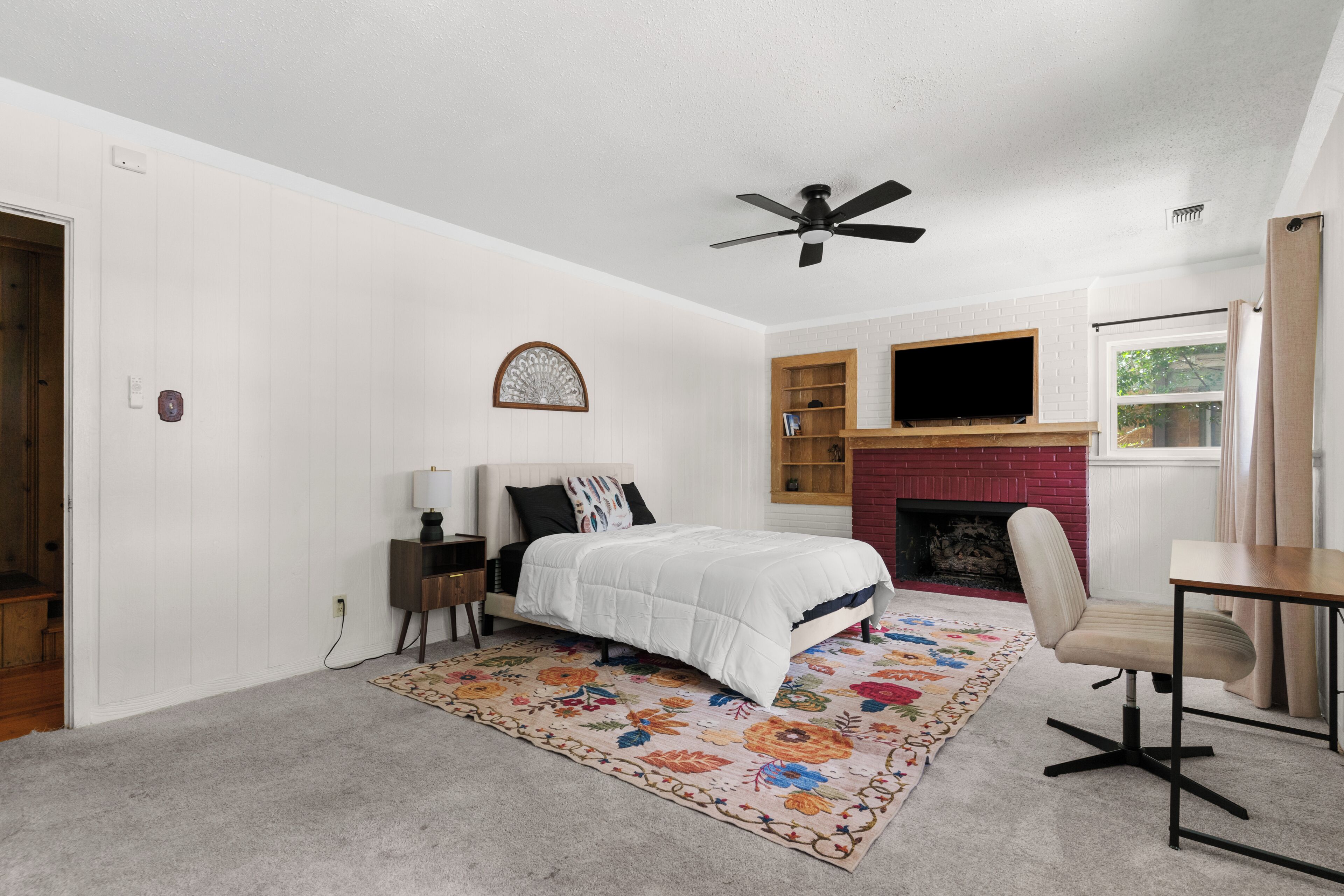Une chambre à coucher comprenant un lit, un bureau, une chaise, une cheminée et un ventilateur de plafond.