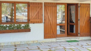 Un edificio con contraventanas de madera, un acceso empedrado y una ventana con vistas a árboles.