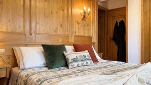 Un dormitorio con paneles de madera, una cama, almohadas, una colcha y una lámpara fijada a la pared.