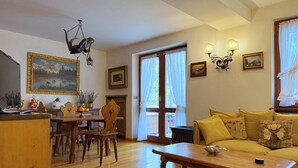 Una sala de estar con una mesa de madera, sillas, un sofá, una chimenea y un ventanal con cortinas.