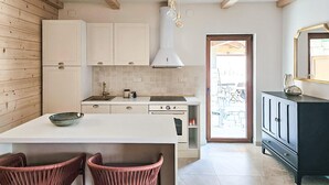 Una cocina con gabinetes blancos, una isla central, una estufa y un comedor con sillas de mimbre.