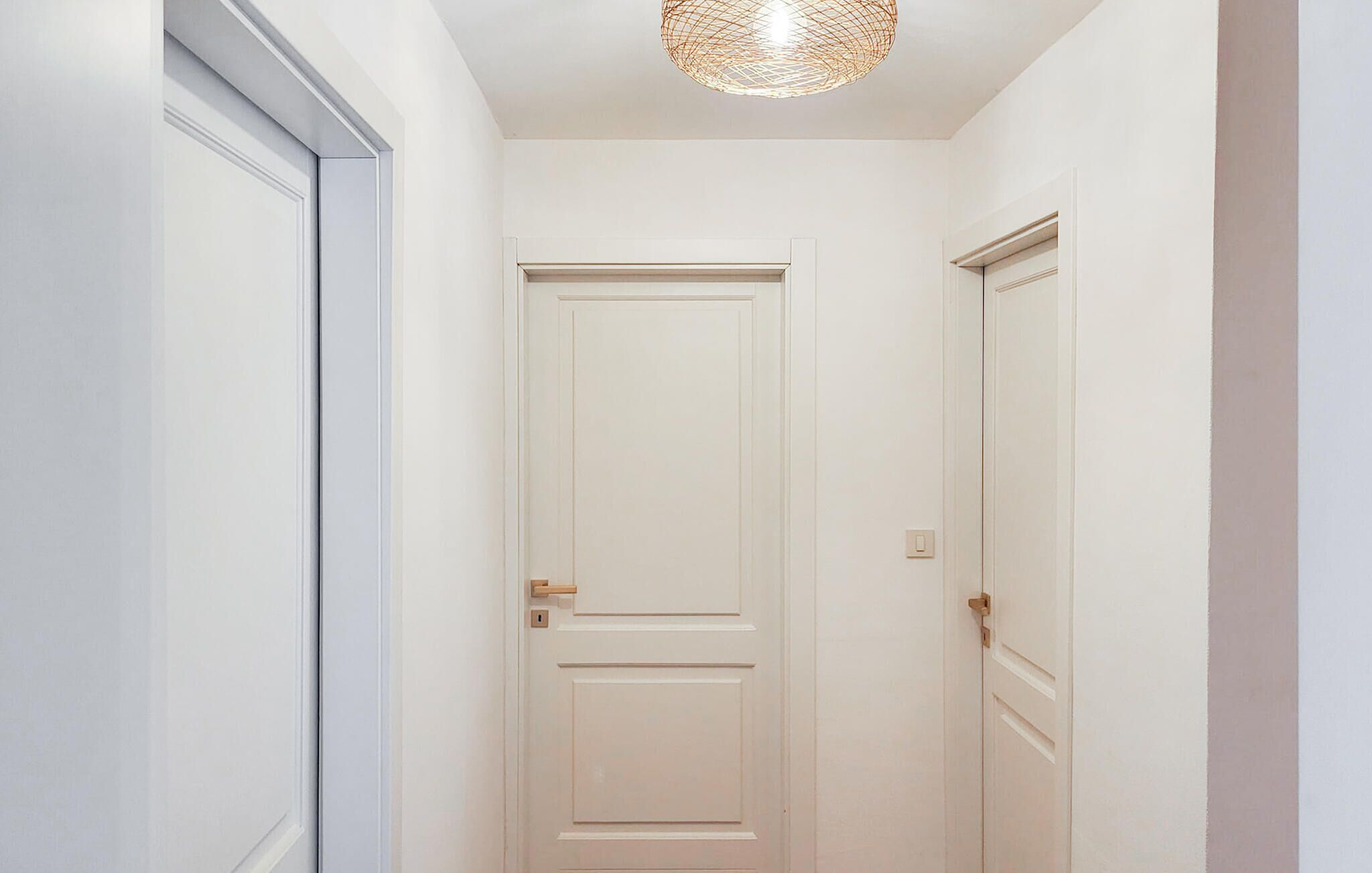 A narrow hallway with white doors, a light switch, and a textured ceiling light fixture.
