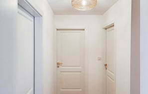 A narrow hallway with white doors, a light switch, and a textured ceiling light fixture. - Lovely home in Smiljan with sauna (Smiljan)