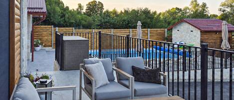 A patio area with outdoor furniture, a pool, and a wooden fence.