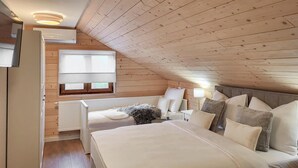 Un dormitorio acogedor en el ático, con techo inclinado, una cama grande, una ventana con persianas y un radiador.